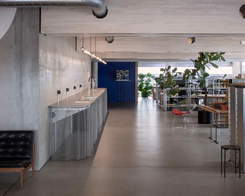 Open office interior with exposed concrete, perforated metal counter, and deep blue wall beyond shelving