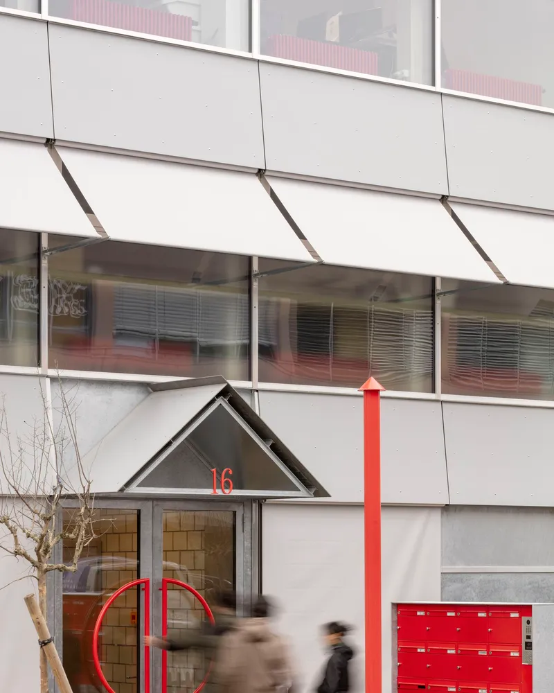 Ground floor entry with triangular canopy, red mailboxes, and blurred pedestrians passing by