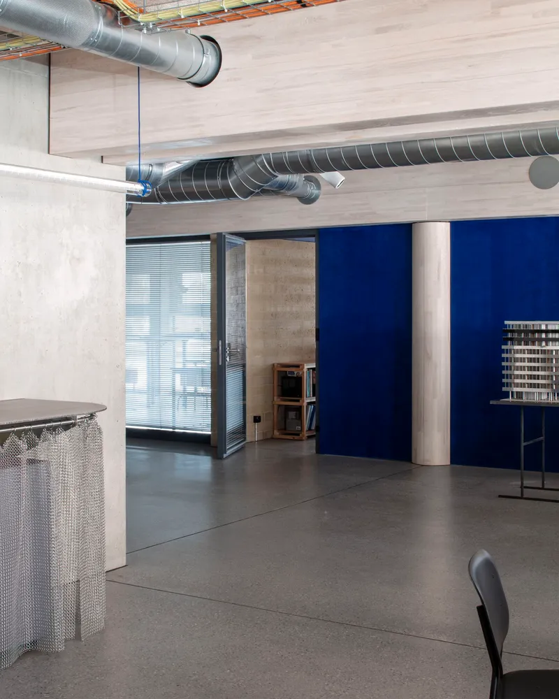 Office interior with exposed spiral ductwork, concrete walls, and blue partition separating work areas