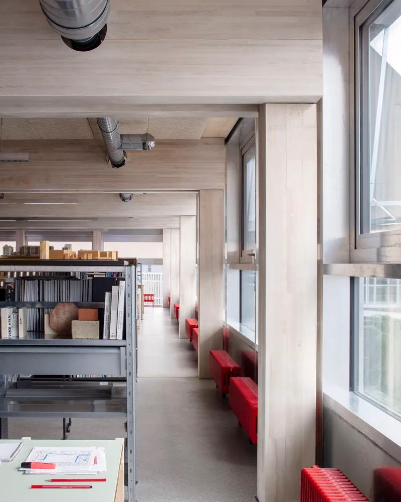 Corridor with timber-lined ceiling, red bench seating along windows, and metal shelving units
