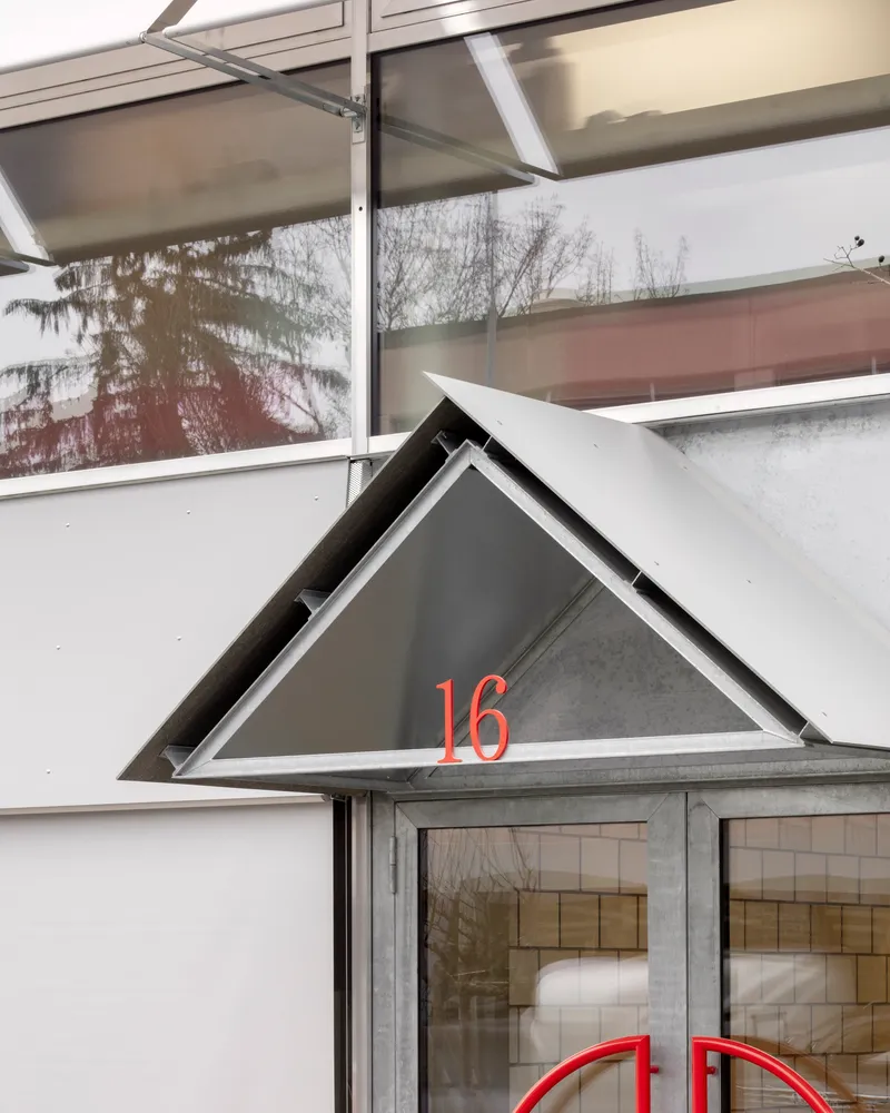 Triangular entry canopy with red numbering above glazed doors and recessed signage