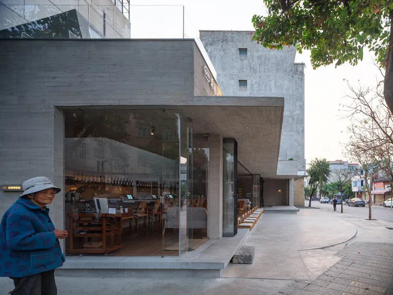 Street corner view of glazed concrete cafe volume with passerby at dusk