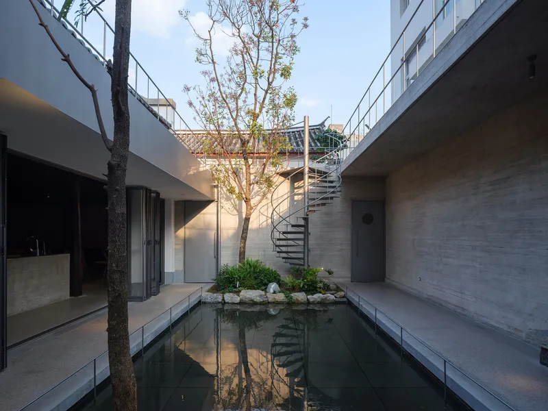 Courtyard pond with spiral staircase and planted tree framed by concrete walls at dusk