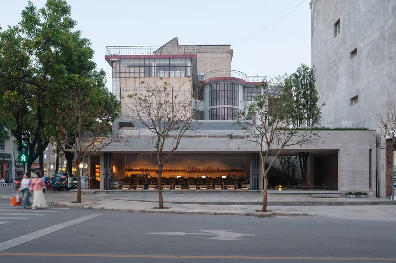 Facade with illuminated interior and pedestrians crossing the street at dusk