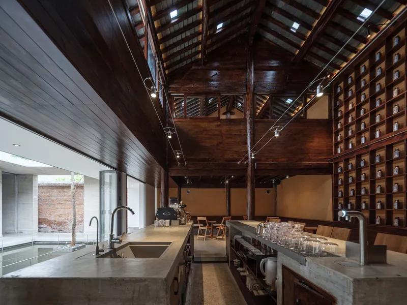 Interior with exposed timber roof structure and stainless steel cafe counter looking toward a planted courtyard
