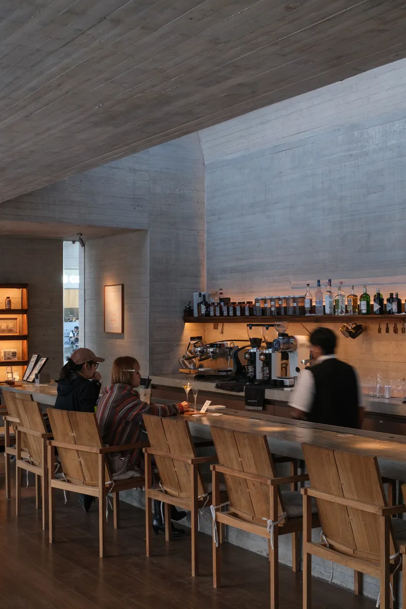 Patrons seated at timber counter under concrete ceiling with angled geometric planes at dusk
