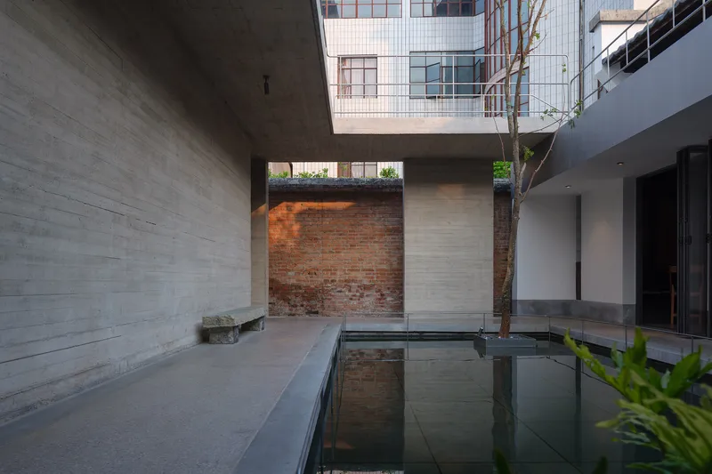 Courtyard water feature with exposed brick wall and tree trunk framed by concrete volumes