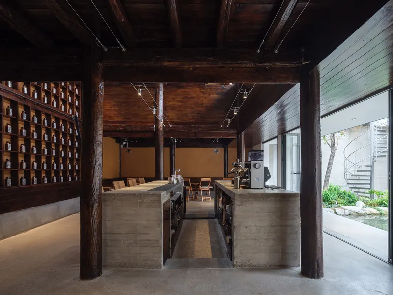 Open kitchen with concrete counters and timber columns beneath exposed ceiling beams with track lighting
