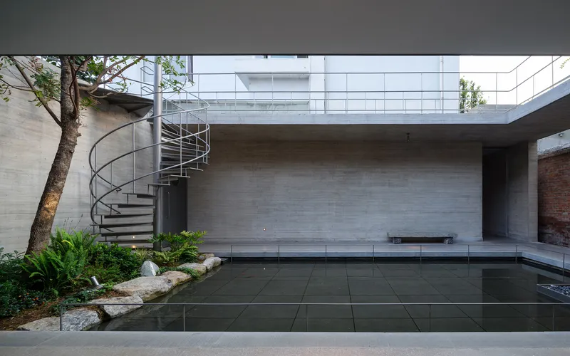 Courtyard with steel spiral staircase beside a board-formed concrete wall and reflecting pool