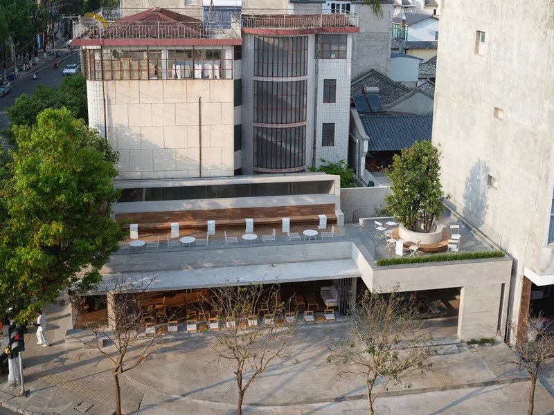 Aerial view showing tiered concrete terraces with timber seating and planted trees between neighboring buildings