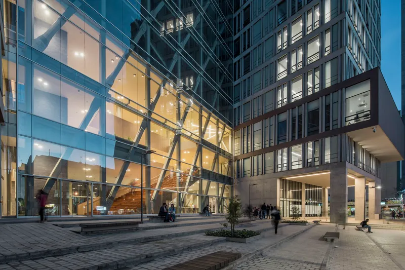 Glass entry pavilion with exposed diagonal bracing and illuminated interior staircase at twilight