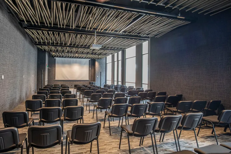 Auditorium with rows of black chairs under an exposed steel and wood batten ceiling