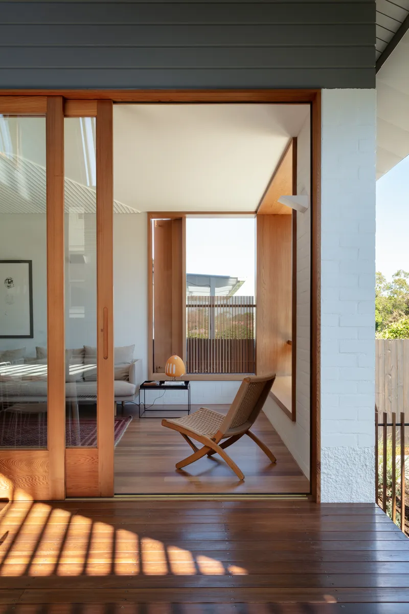 Timber-framed glazed doorway opening from exterior deck to bedroom with folding chair and slatted screen