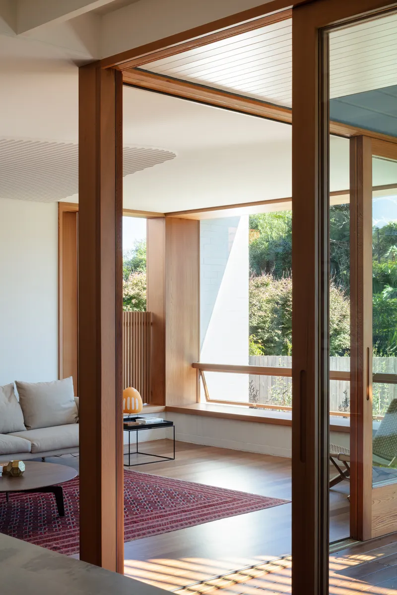 Timber-framed doorway opening from a living room onto a sunny terrace with garden views