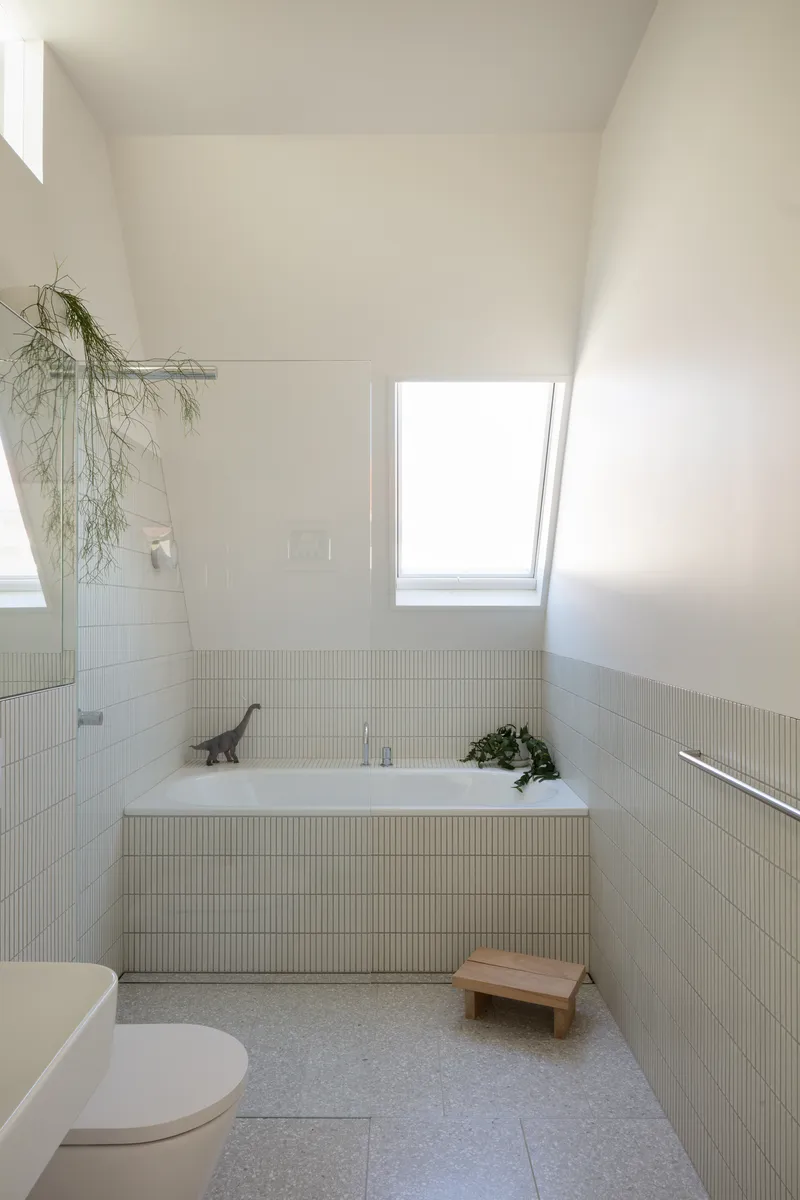 Bathroom with fluted tile wainscoting, built-in bathtub, and skylight above