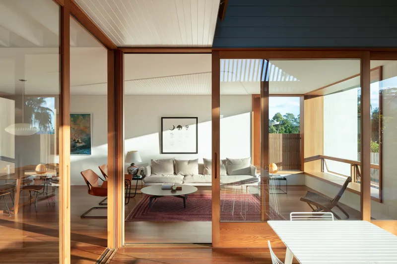 Timber-framed glazed doors opening from deck to living room with beadboard ceiling in afternoon light