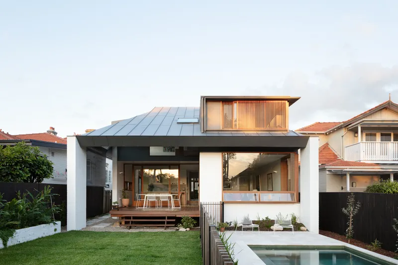 Rear facade with metal roof and timber screening above pool and lawn at dusk
