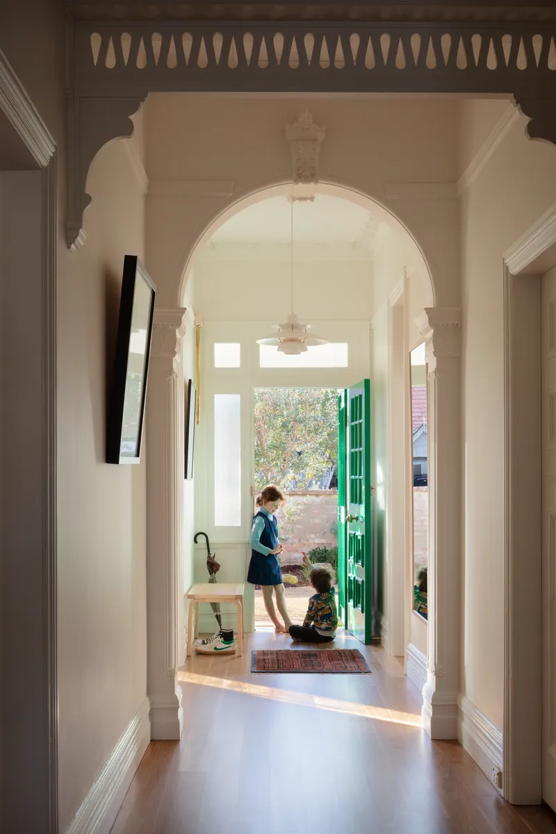 View through arched doorway and hallway toward bright green entry door with two children inside