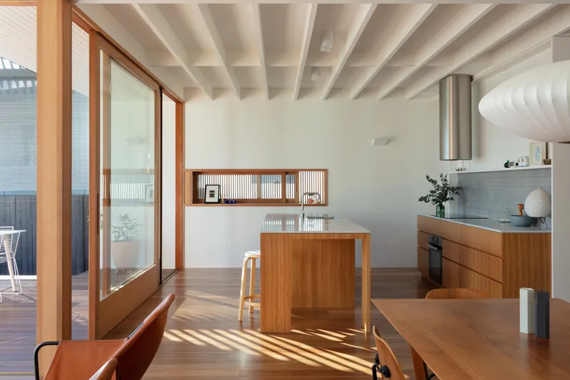 Open kitchen and dining space with timber island and exposed white ceiling beams in morning light