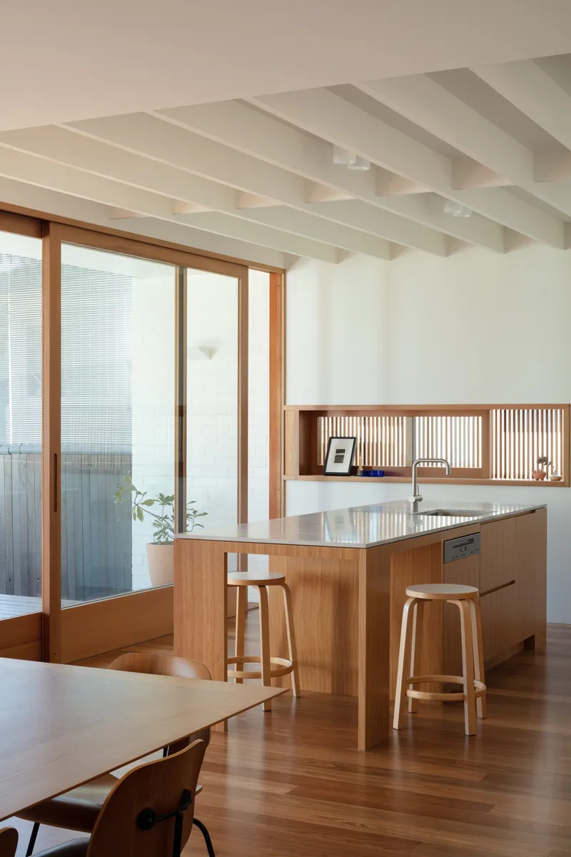 Kitchen island with timber cabinetry and slatted shelving niche beneath white painted ceiling beams