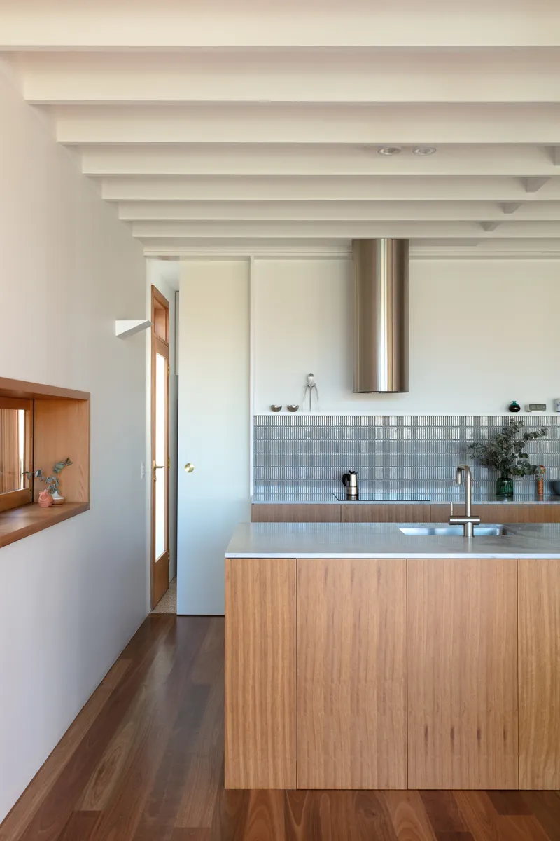 Kitchen counter with grey mosaic tile backsplash and timber veneer cabinetry under exposed white beams