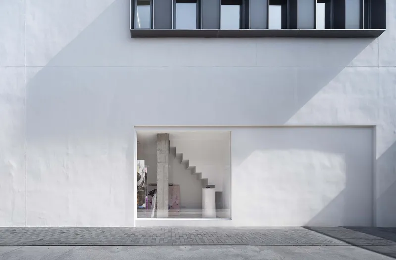 Street view through large glazed opening revealing concrete stair and column in afternoon light