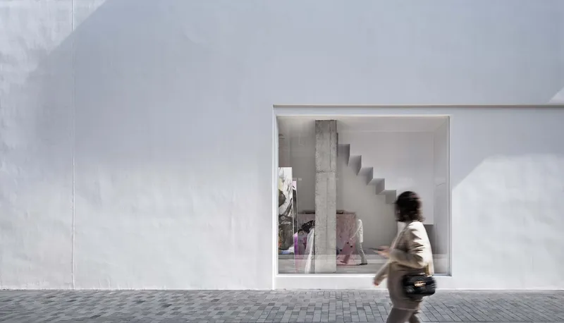 Pedestrian passing the storefront window framing interior stair and concrete column in shadow