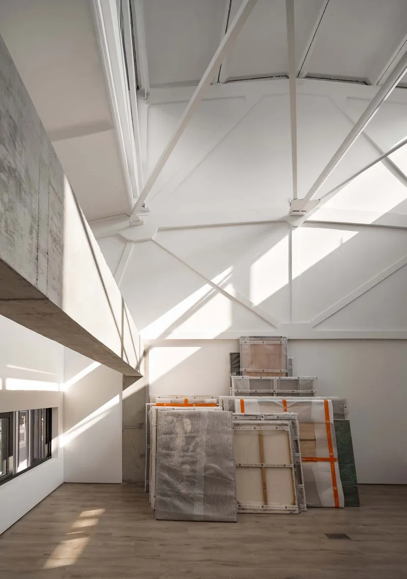 Double-height gallery space with exposed white steel trusses and stacked canvases on timber floor