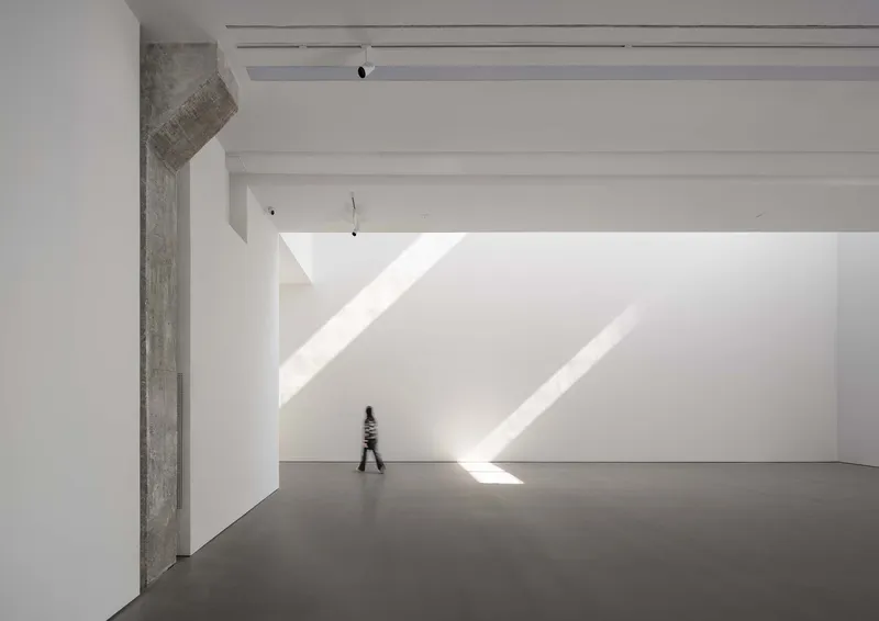 Gallery hall with raw concrete column and figure walking through diagonal sunlight on floor