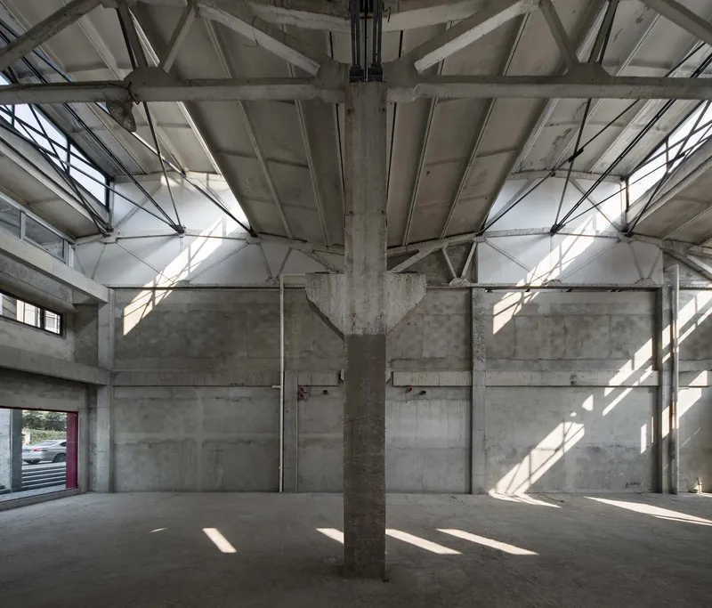 Exposed concrete structure with central column and steel roof trusses in bright natural light