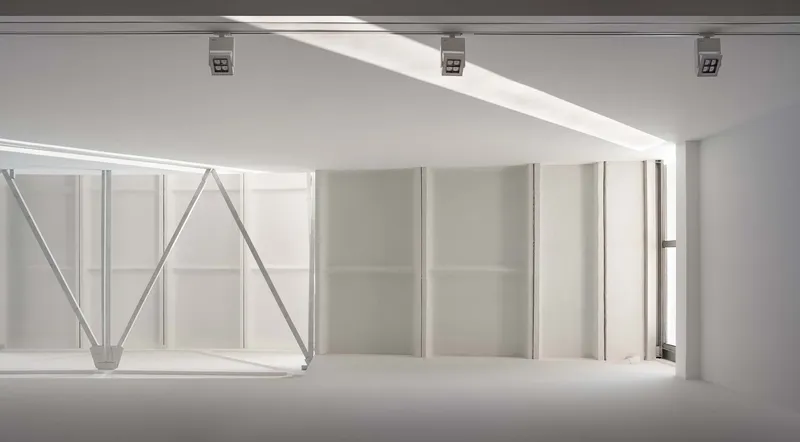 Gallery space with exposed steel truss structure and white partition walls below a clerestory