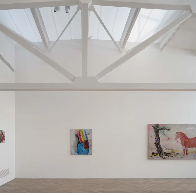 Interior gallery with exposed steel roof trusses and skylights above paintings on white walls
