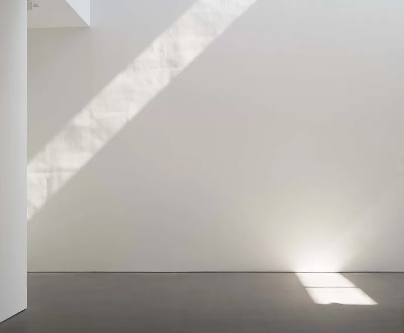 White interior corner with diagonal shadows cast by unseen skylight above grey concrete floor