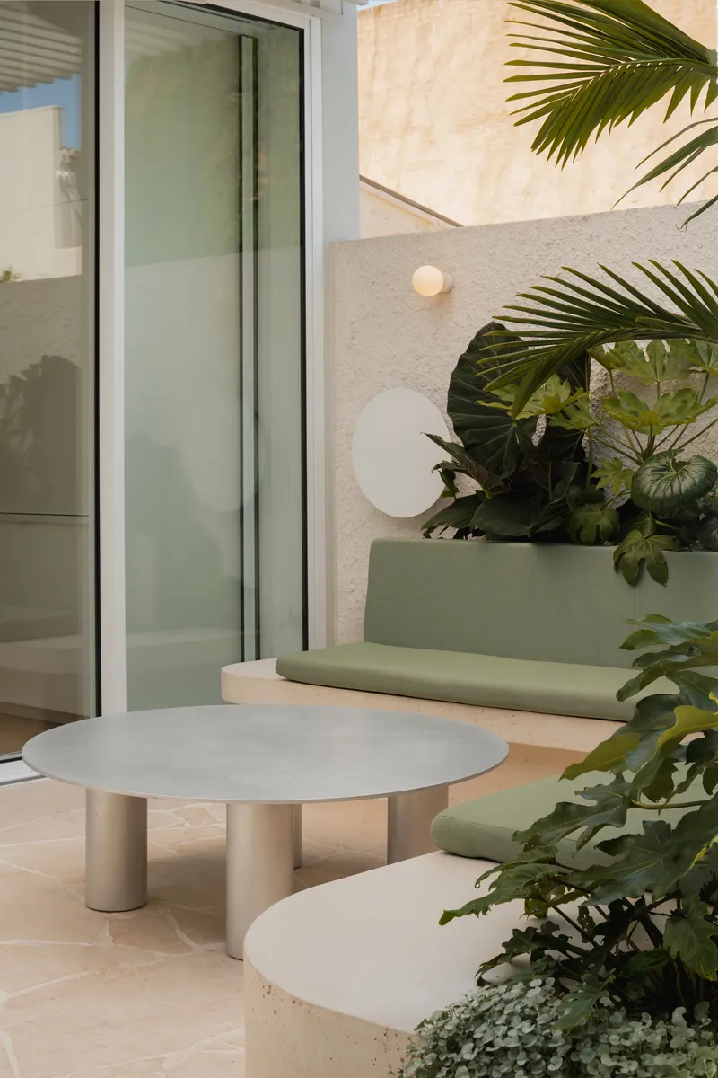 Courtyard terrace with pale stone table and built-in sage green bench beside tropical planting