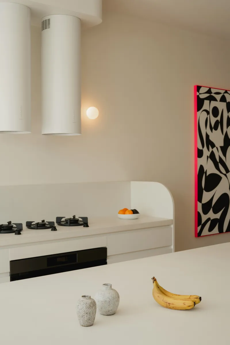 Kitchen counter with white cylindrical range hood and bananas on the surface below pendant light
