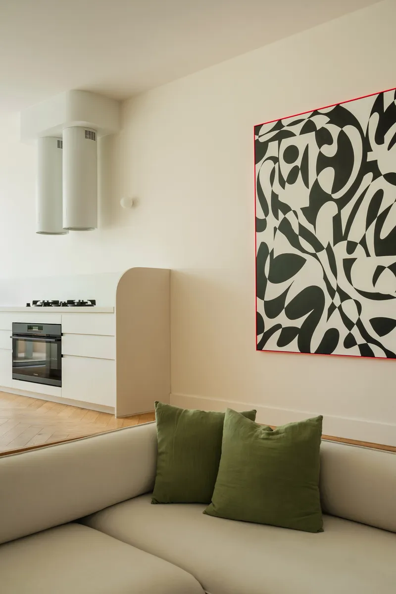 Living space with open kitchen and abstract artwork above sofa with green cushions