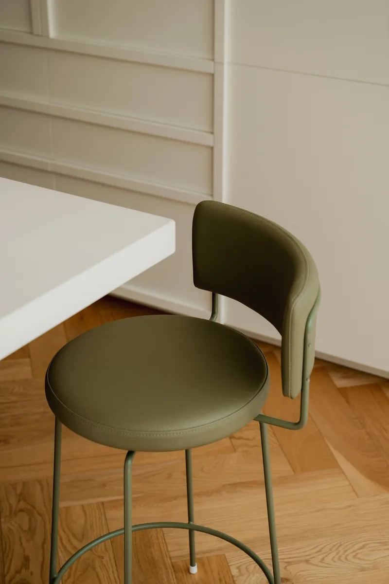 Olive green upholstered chair with curved backrest tucked beneath a white table on herringbone timber floor