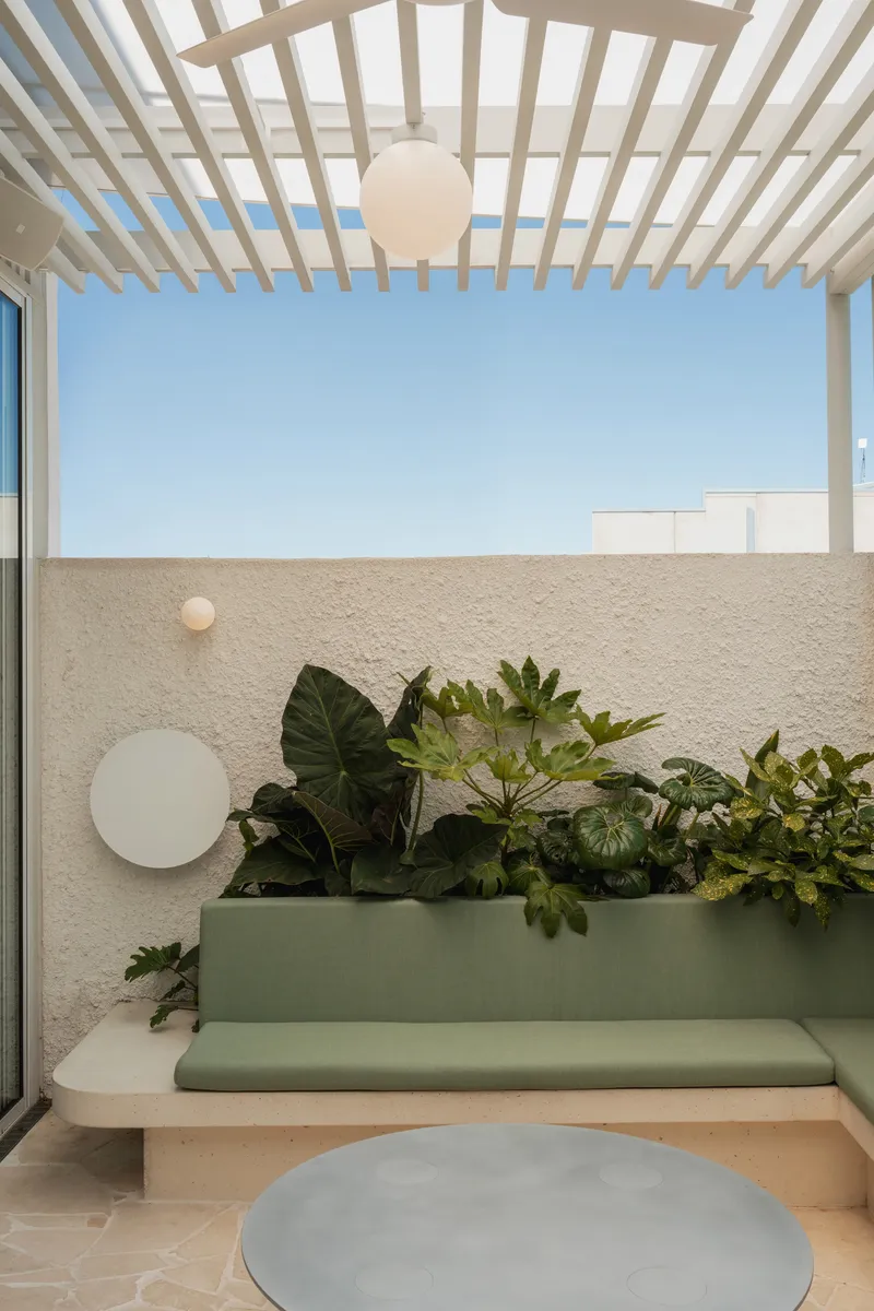 Covered terrace with timber slat pergola, integrated bench, planted bed, and spherical pendant light at dusk