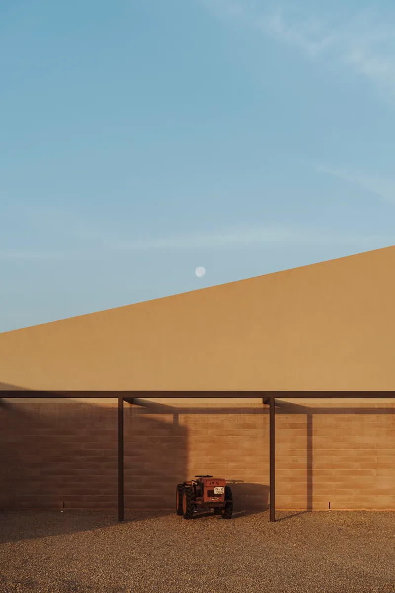 Covered carport with slender steel columns and timber screening panels beneath a fading moon