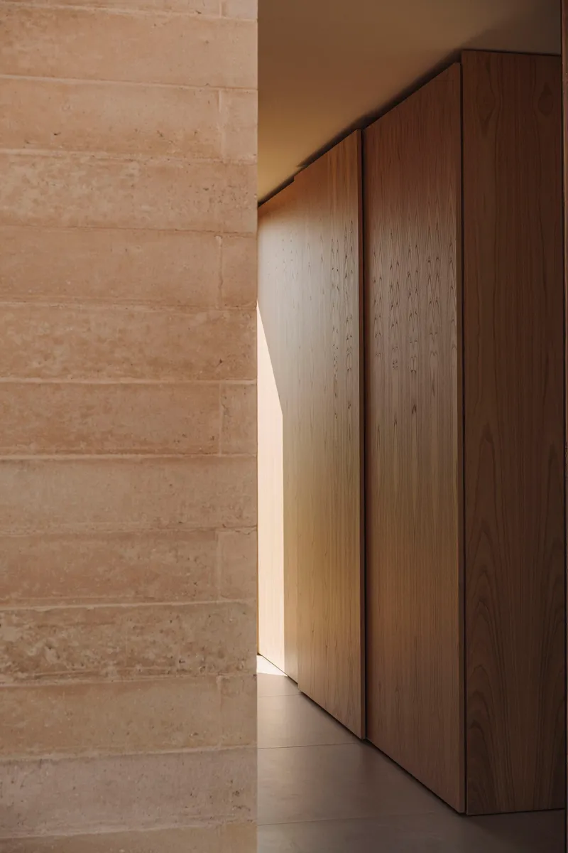 Close-up of timber cabinetry meeting a rammed earth wall in soft natural light
