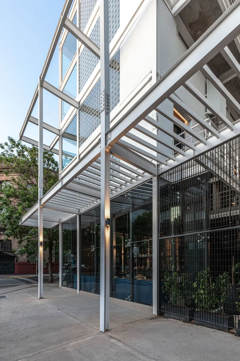 Ground level covered entry with steel pergola structure and vertical metal bar screens beside planted areas