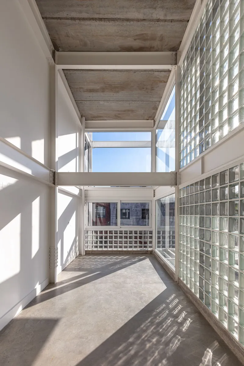 Interior balcony with exposed concrete ceiling and glass block wall casting geometric shadows on polished floor