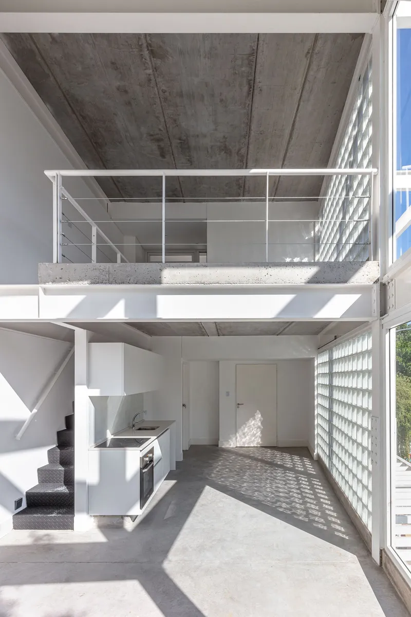 Double height interior space with mezzanine, exposed concrete ceiling and kitchen beneath upper level railing