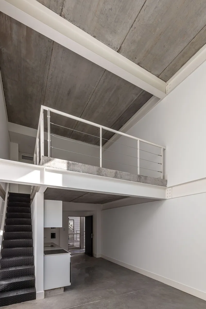 Double-height interior with mezzanine, exposed concrete ceiling and metal railing