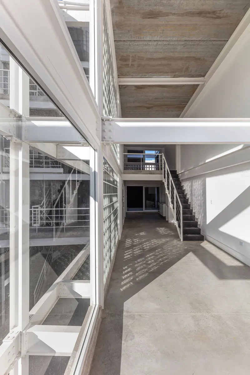 Interior hallway with glass block wall and overlapping steel staircases in afternoon light