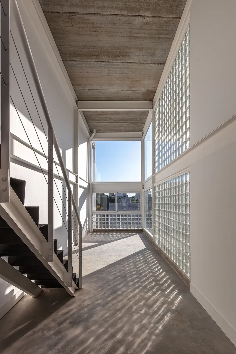 Interior corridor with board-formed concrete ceiling and glass block wall casting patterned shadows across the floor