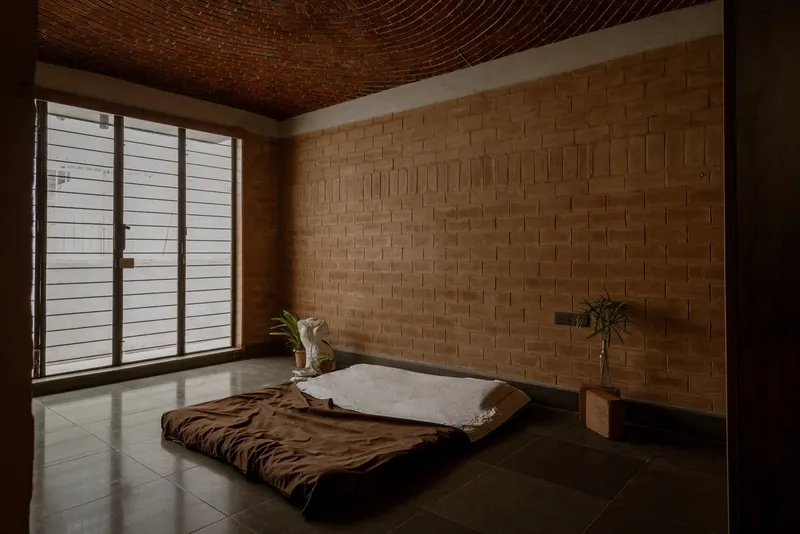Sleeping room with low platform bed beneath basket-weave brick vault and horizontal louvered window