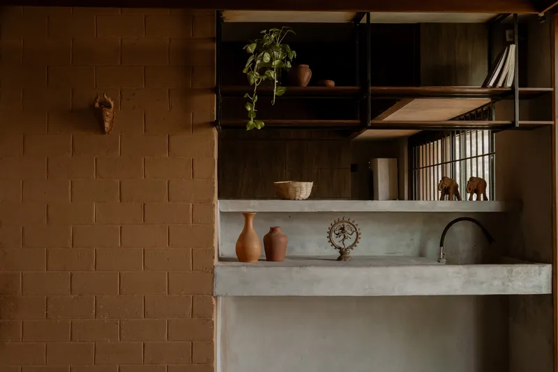Close-up of concrete countertop with pottery vessels and timber shelving against sandstone block wall