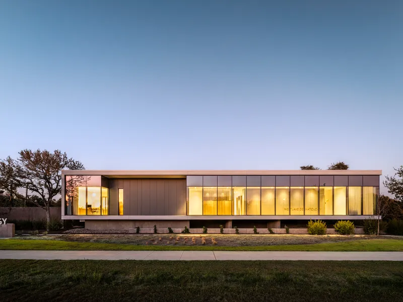 Long facade combining glazing and paneled cladding with warm interior lighting visible at twilight
