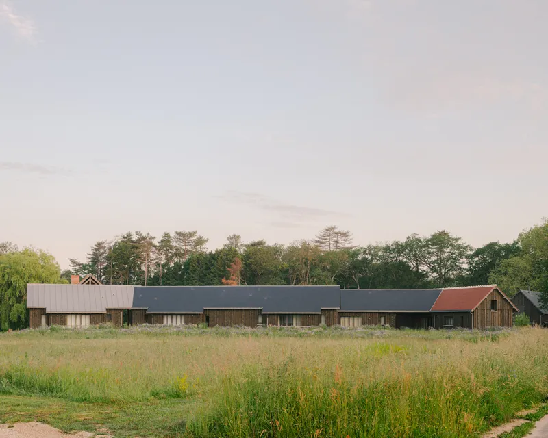 Linear timber-clad volume with varied rooflines set in a wildflower meadow at dusk